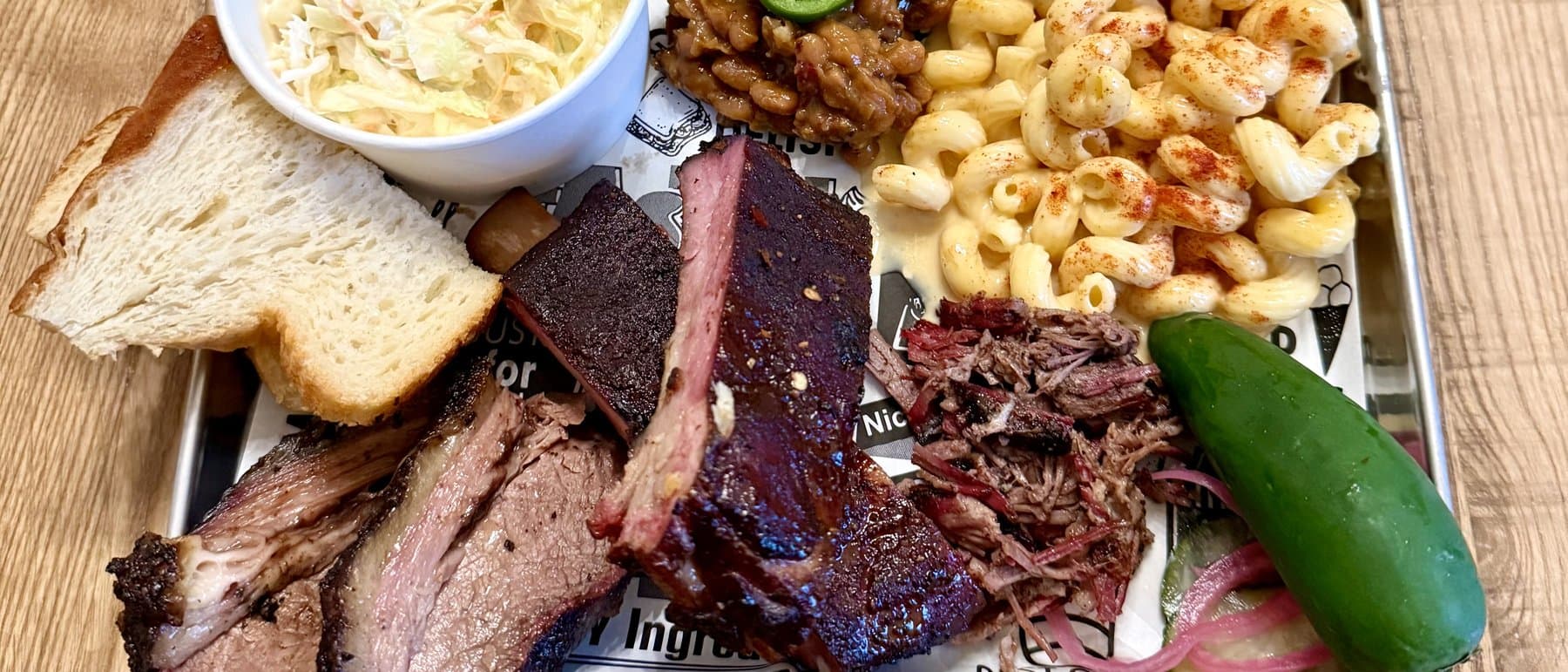 Que17 barbecue tray with brisket, ribs, pulled pork, mac and cheese, beans, slaw, and house pickles